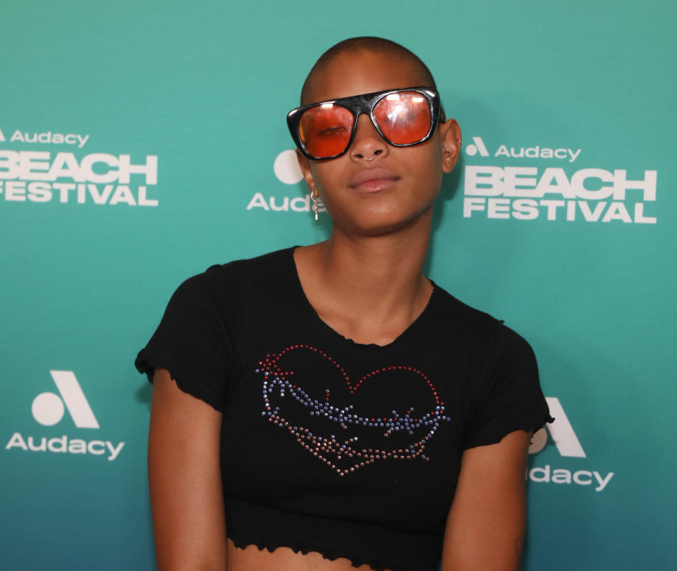 Person with orange-tinted sunglasses and a black top with rhinestone heart design at Audacy Beach Festival