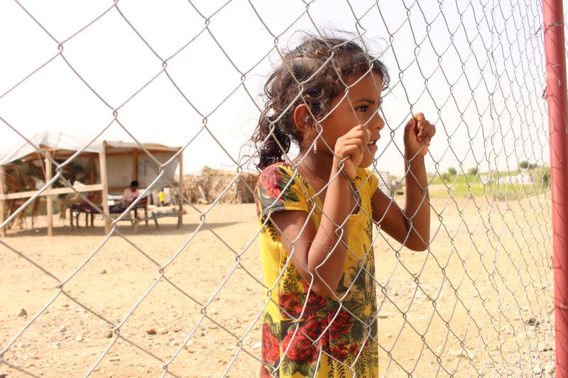 Girl looks from behind a fence of a medical centre of a camp for internally displaced in Abs of Hajja province