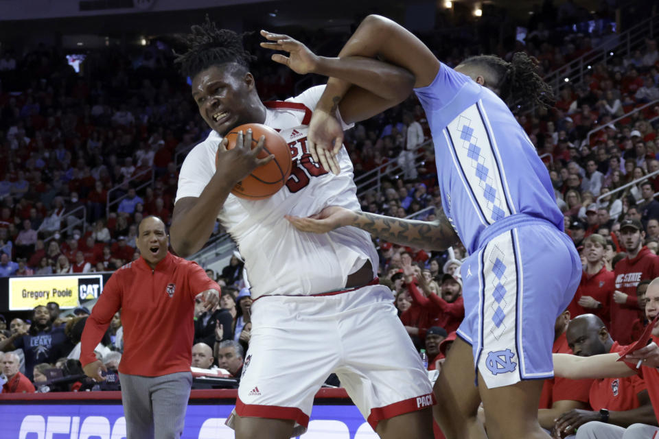 North Carolina State head coach Kevin Keatts, back left, reacts as North Carolina State forward D.J. Burns Jr., center, battles North Carolina forward Armando Bacot, right, for the ball during the second half of an NCAA college basketball game, Sunday, Feb. 19, 2023, in Raleigh, N.C. (AP Photo/Chris Seward)