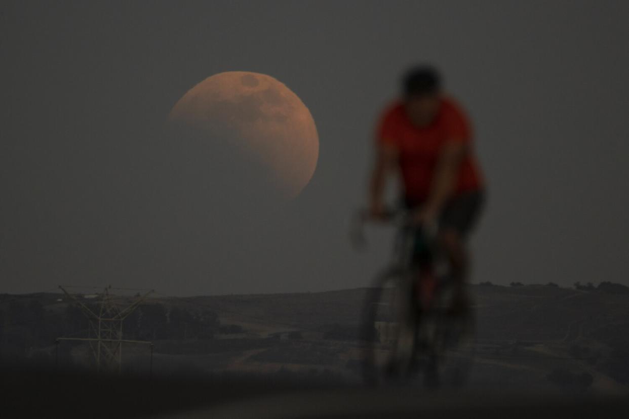 A person on a bicycle with a red moon behind them