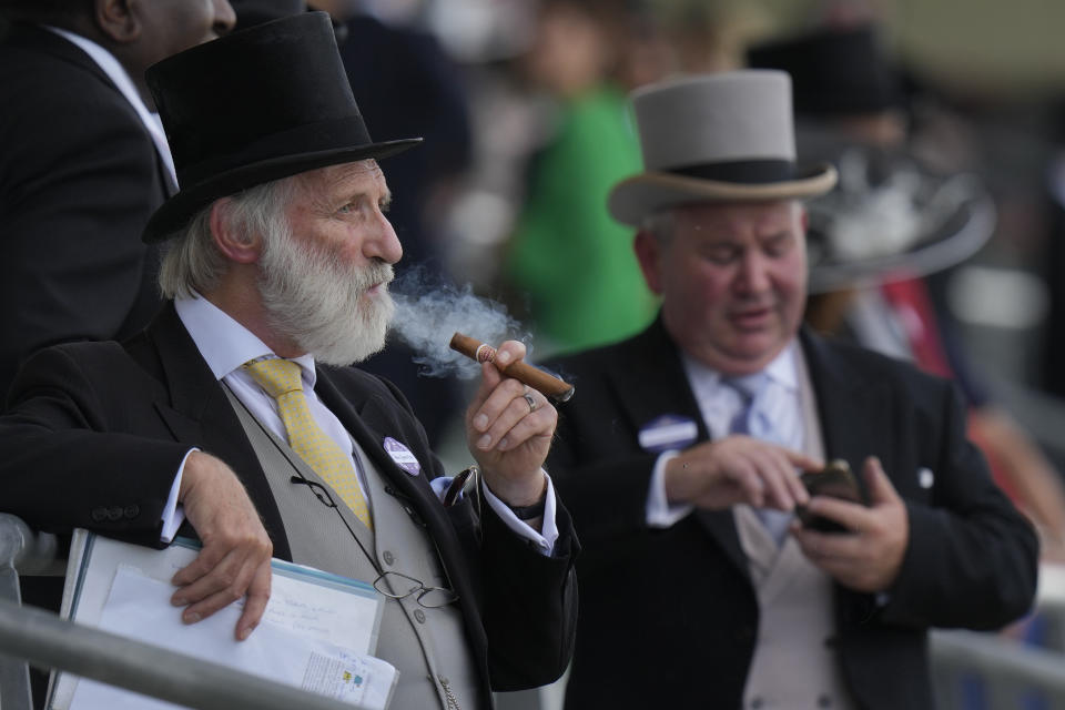 A racegoer smokes a cigar as he studies the form on the second day of of the Royal Ascot horserace meeting, at Ascot Racecourse, in Ascot, England, Wednesday, June 15, 2022. (AP Photo/Alastair Grant)