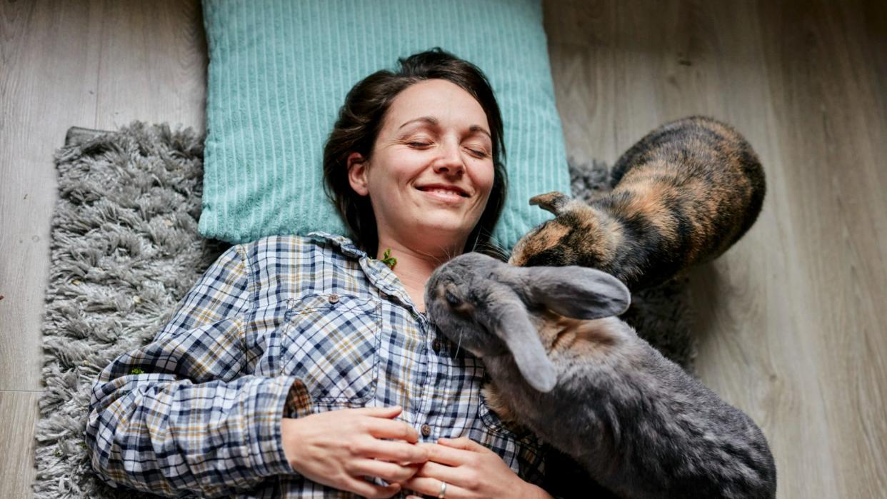  Woman lying on floor with two pet rabbits. 