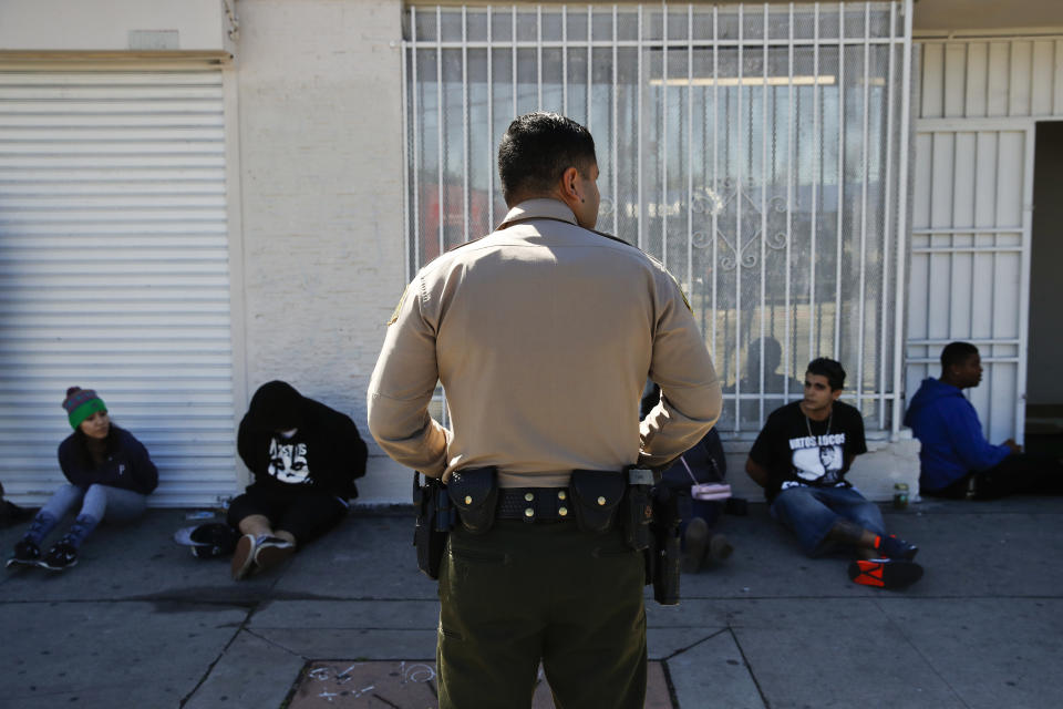 FILE - In this March 15, 2018 file photo, a Los Angeles County Sheriff's deputy keeps watch on a group of people apprehended at an illegal marijuana dispensary in Compton, Calif. The number of felony marijuana arrests in California continued to plunge in 2019 in the age of legalization, but another trend remained unchanged: those arrests fell disproportionately on Hispanics and Blacks, state data showed. (AP Photo/Jae C. Hong, File)