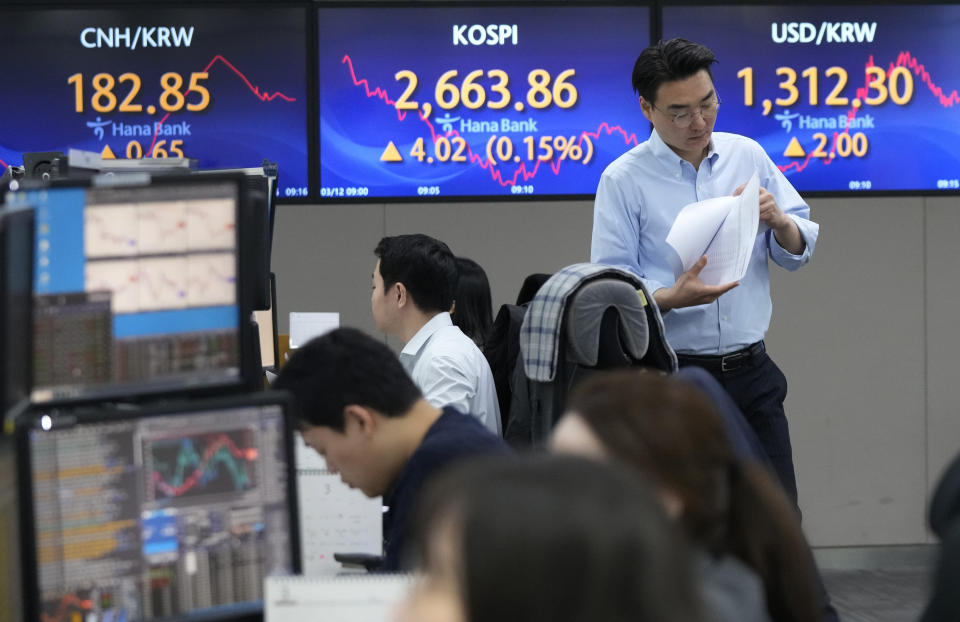 A currency trader passes by the screens showing the Korea Composite Stock Price Index (KOSPI), center, and the foreign exchange rate between U.S. dollar and South Korean won, right, at the foreign exchange dealing room of the KEB Hana Bank headquarters in Seoul, South Korea, Tuesday, March 12, 2024. Shares were mostly higher in Asia on Tuesday ahead of a report on inflation in the U.S. that could sway the Federal Reserve’s timing on cutting interest rates. (AP Photo/Ahn Young-joon)