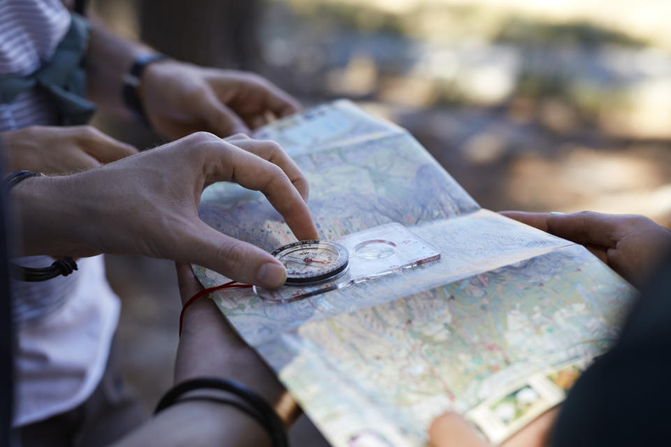 Close-up of hands holding compass & map, in forest