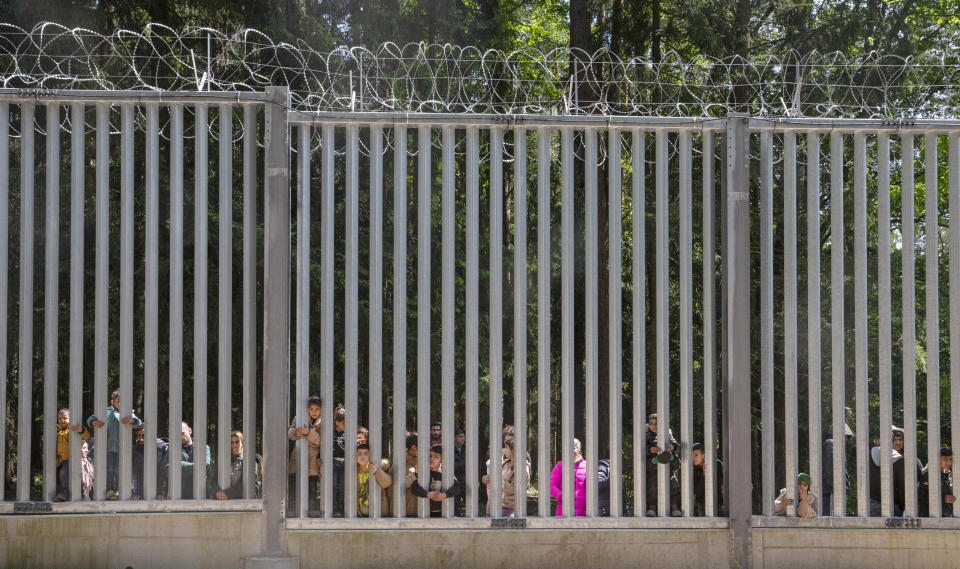 FILE - Members of a group of some 30 migrants seeking asylum look through the railings of a wall that Poland has built on its border with Belarus to stop massive migrant pressure, in Bialowieza, Poland, on May 28, 2023. Poland’s conservative governing party was hoping to make migration a key campaign theme ahead of the country’s national election. But not like this. The Law and Justice party is being rocked by reports that Polish consulates issued visas in Africa and Asia in exchange for bribes, opening the door for migrants to enter the European Union. (AP Photo/Agnieszka Sadowska, File)