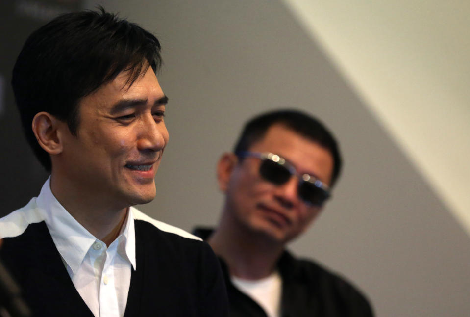 Movie director Wong Kar-wai, right, watches from the background as Tony Leung, left, speaks during a press conference on Wednesday, Jan. 23, 2013 in Singapore. For a director and actor who have worked together for about two decades, there did not seem to be much chemistry between Wong and Leung at the news conference promoting their new movie "The Grandmaster." (AP Photo/Wong Maye-E)