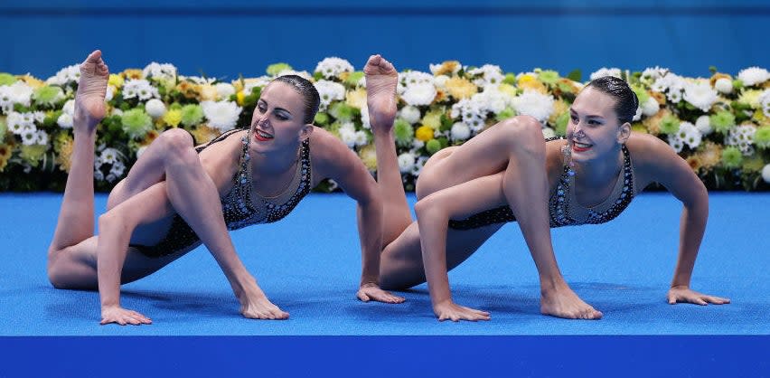 The synchronized swimmers each have a leg twisted over an arm as they crouch on the ground