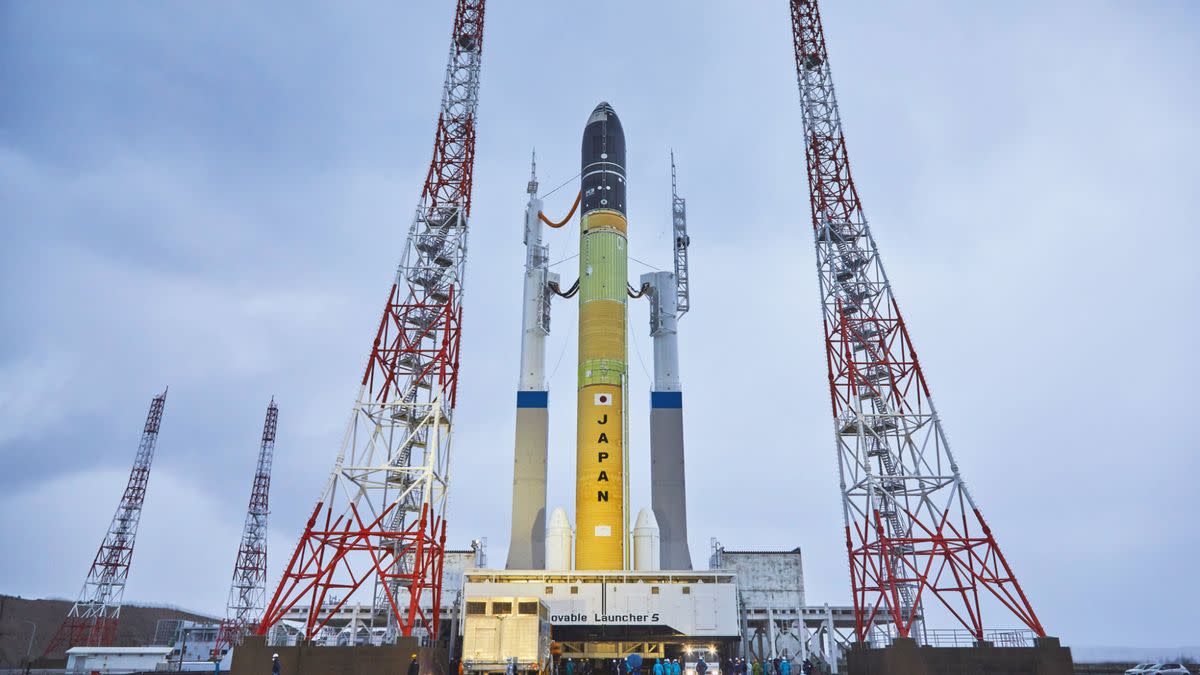  A rocket sits on a launch pad in between towers with cloudy sky in behind. 