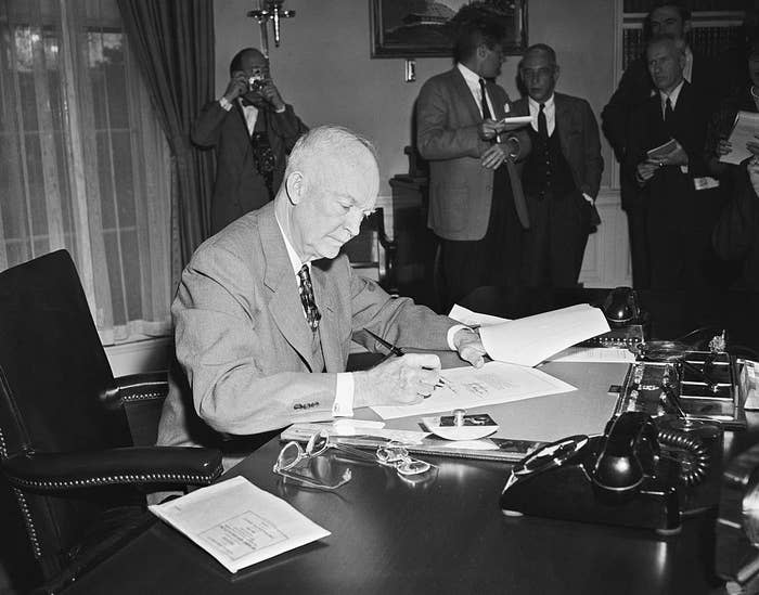Eisenhower signing a document while other government officials stand by