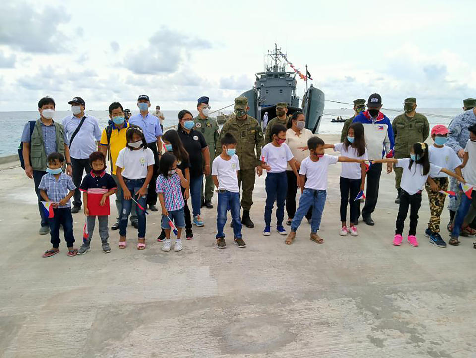 In this handout photo provided by the Department of National Defense PAS, Defense Secretary Delfin Lorenzana, 4th from right, and the other military officials are welcomed by residents wearing masks during a short ceremony at the newly built beach ramp at the Philippine-claimed island of Pag-asa, also known as Thitu, in the disputed South China Sea on Tuesday June 9, 2020. The Philippine defense chief and top military officials flew to a disputed island in the South China Sea Tuesday to inaugurate a beach ramp built to allow the "full-blast" development of the far-flung territory but would likely infuriate China. (Department of National Defense PAS via AP)