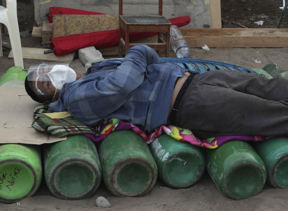 A man sleeps on top of empty oxygen cylinders, waiting for a shop to open to refill his tank, in the Villa El Salvador neighborhood of Lima, Peru, early Thursday morning, Feb. 18, 2021. A crisis over the supply of medical oxygen for coronavirus patients has struck nations in Africa and Latin America, where warnings went unheeded at the start of the pandemic and doctors say the shortage has led to unnecessary deaths. (AP Photo/Martin Mejia)