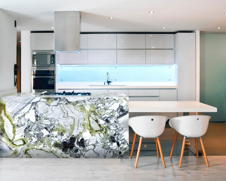 Modern kitchen space with stand out kitchen island in white beauty marble, seating at the lower level of the island, white kitchen cabinets, grey flooring