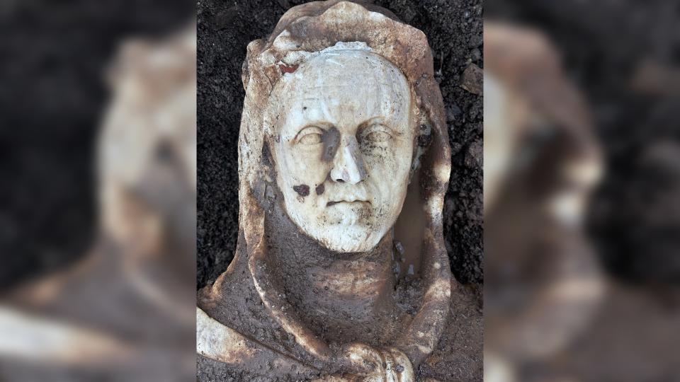 The head of the statue showing the Roman emperor against the dirt-covered ground.