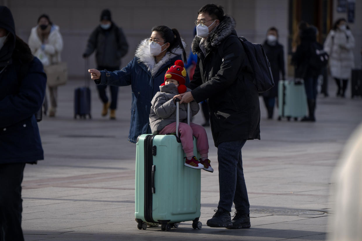 Travelers wearing face masks roll their suitcase toward the entrance of the Beijing Railway Station in Beijing, Saturday, Jan. 14, 2023. Millions of Chinese are expected to travel during the Lunar New Year holiday period this year. (AP Photo/Mark Schiefelbein)