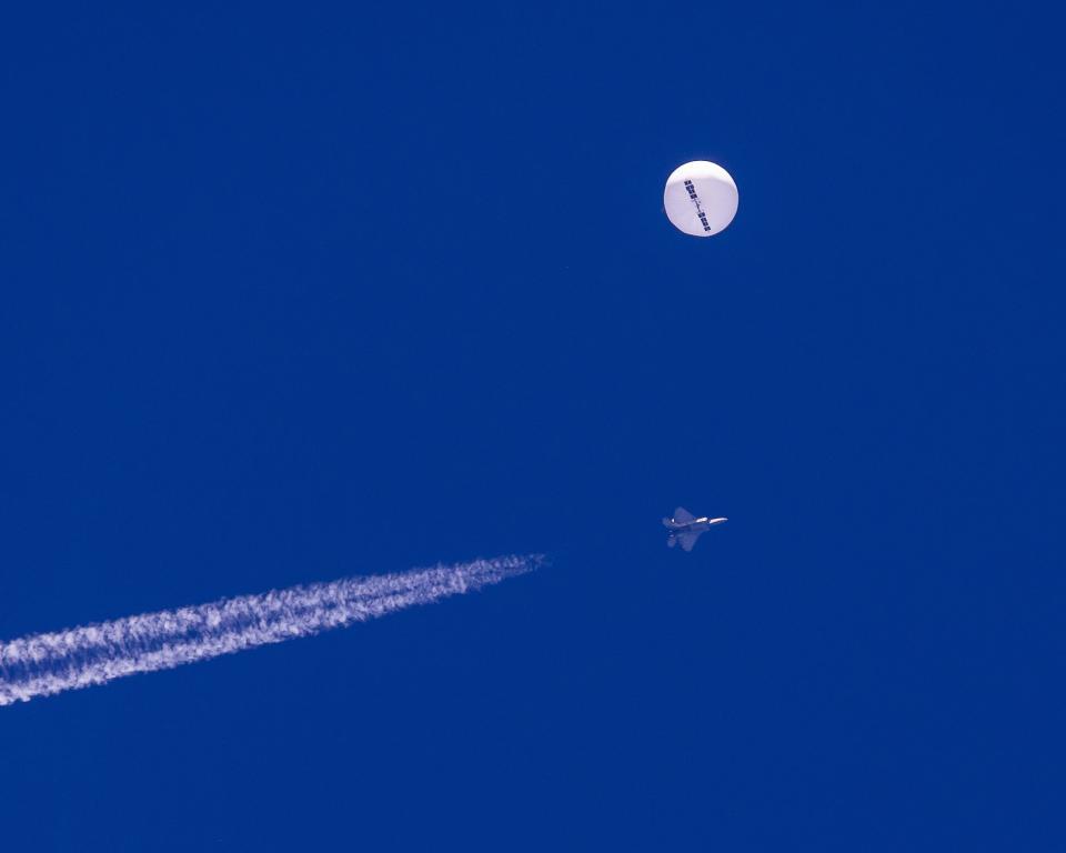 In this photo provided by Chad Fish, a large balloon drifts above the Atlantic Ocean, just off the coast of South Carolina, with a fighter jet and its contrail seen below it, Saturday. The balloon was struck by a missile from an F-22 fighter just off Myrtle Beach.