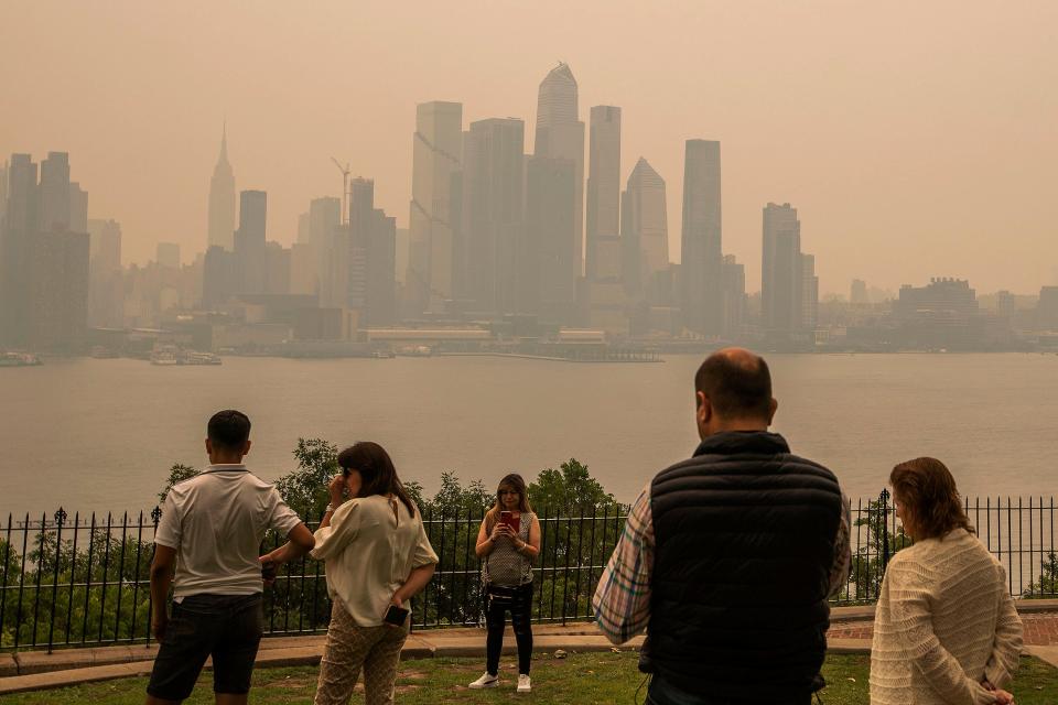 : Les gens se tiennent dans un parc alors que l'horizon de New York est couvert de brume et de fumée des incendies de forêt au Canada le 7 juin 2023 à Weehawken, New Jersey