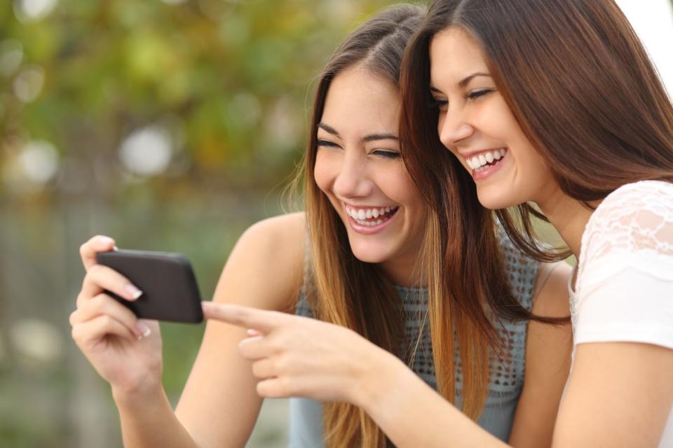 Two people laughing while watching a video on a smartphone.