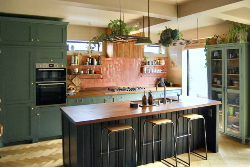 Kitchen with large wooden island with green cabinets and terracotta backsplash.