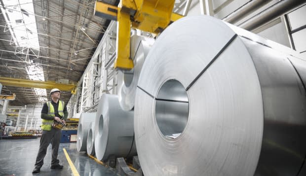 Worker operating crane with steel rolls in car factory