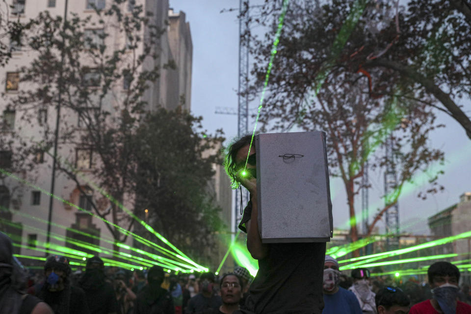 Anti-government demonstrators shine laser pointers a the police during a protest in Santiago, Chile, Thursday, Nov. 14, 2019. Students in Chile began protesting nearly a month ago over a subway fare hike. The demonstrations have morphed into a massive protest movement demanding improvements in basic services and benefits, including pensions, health, and education. (AP Photo/Esteban Felix)