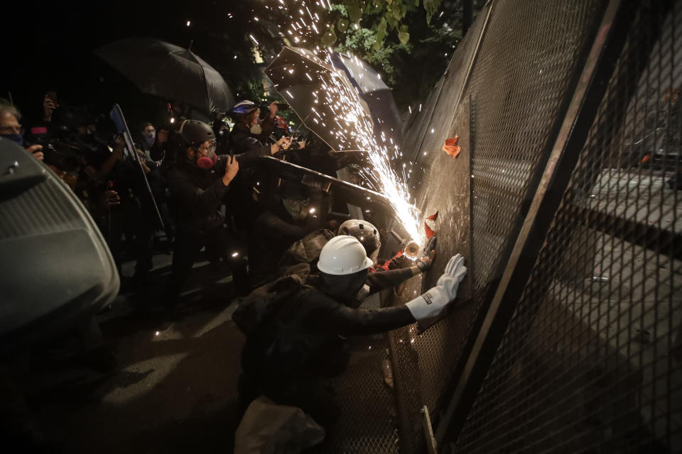 Demonstrators try to cut through a steel fence during a Black Lives Matter protest at the Mark O. Hatfield U.S. Courthouse on Friday, July 24, 2020, in Portland, Ore. On the streets of Portland, a strange armed conflict unfolds night after night. It is raw, frightening and painful on both sides of an iron fence separating the protesters on the outside and federal agents guarding a courthouse inside. This weekend, journalists for The Associated Press spent the weekend both outside, with the protesters, and inside the courthouse, with the federal agents, documenting the fight that has become an unlikely centerpiece of the protest movement gripping America. (AP Photo/Marcio Jose Sanchez)
