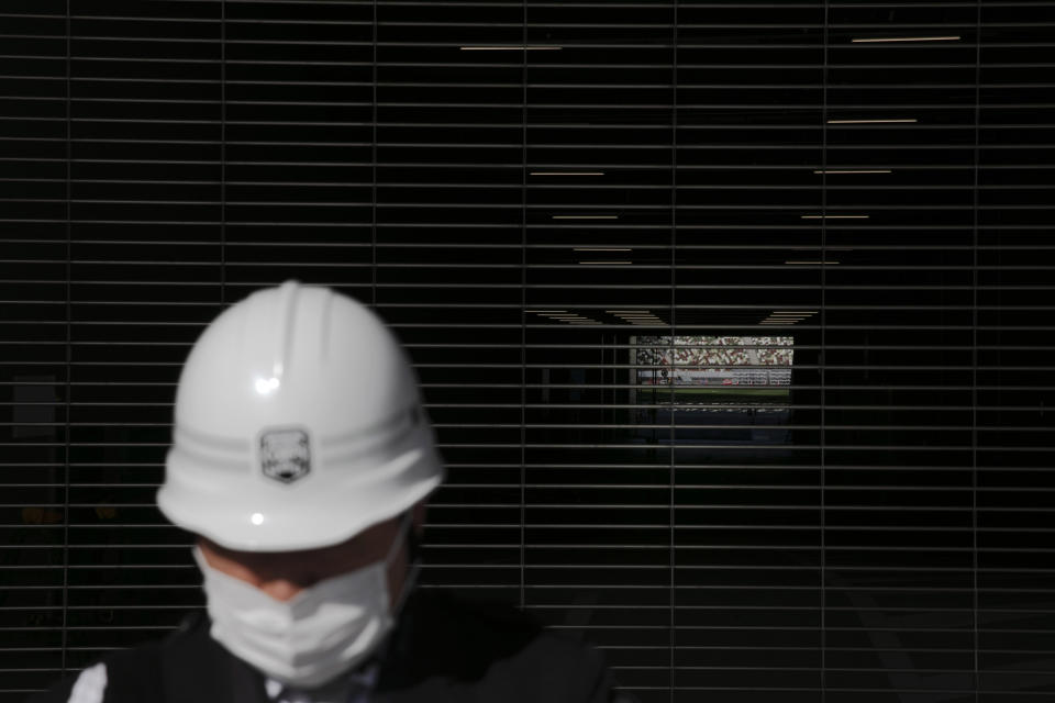 A security guard with a mask stands in front of a tunnel leading to the field of the New National Stadium, a venue for the opening and closing ceremonies at the Tokyo 2020 Olympics, Sunday, Feb. 23, 2020, in Tokyo. (AP Photo/Jae C. Hong)