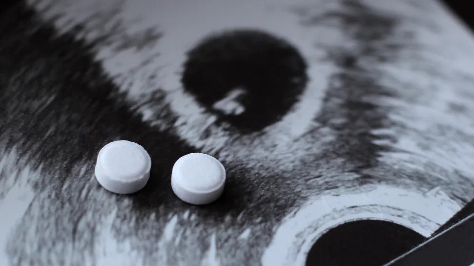 Two white round abortion medication pills on top of a black-and-white sonogram of a baby.