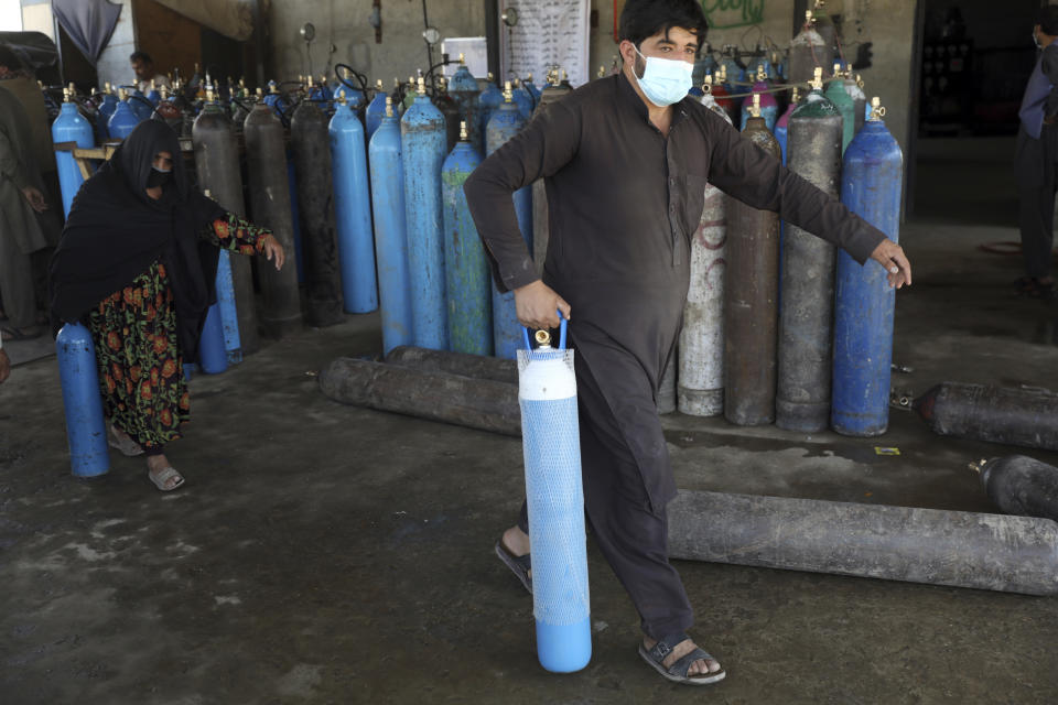 A man and woman carry an oxygen cylinders from a privately owned oxygen factory, in Kabul, Afghanistan, Saturday, June 19, 2021. Health officials say Afghanistan is fast running out of oxygen as a deadly third surge of COVID worsen. (AP Photo/Rahmat Gul)