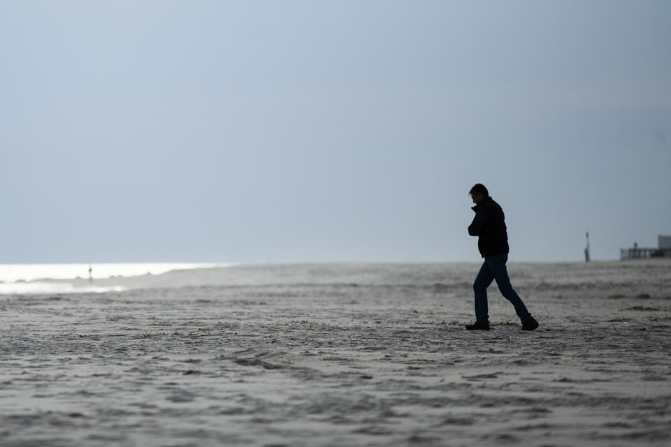 FILE - In this March 18, 2020, file photo, a person walks toward the ocean in Cape May, N.J. As the weather warms, some already have begun venturing outside, despite guidance to stay home. Government officials say they aim to manage public health risks in a way that allows for a gradual return to normal, but with the course of the outbreak still unknown, nobody is sure what summer will bring. (AP Photo/Matt Rourke, File)