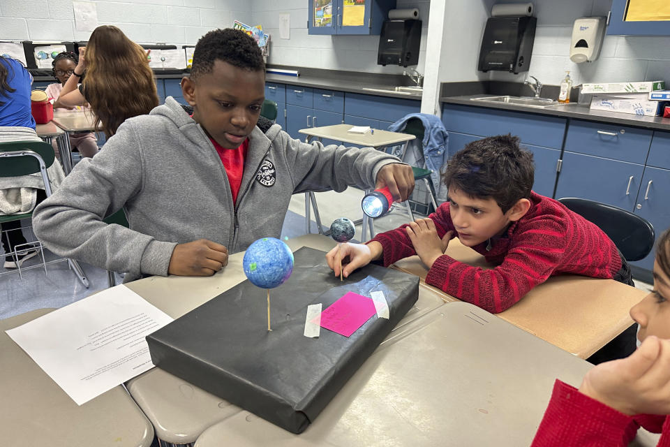 Alex Impion, 12, shines a flashlight on a model moon held by Necmeddin Aljabri, 8, at Riverside Elementary School in Cleveland on March 14, 2024. The two were learning about the upcoming total solar eclipse, a topic that has challenged and inspired teachers in and near the eclipse's path. (AP Photo/Carolyn Thompson)