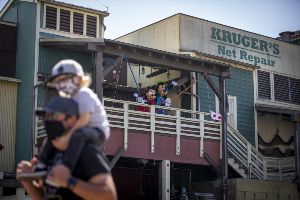 Disney characters Goofy and Max on a balcony with, in the foreground, a man carrying a child on his shoulders.