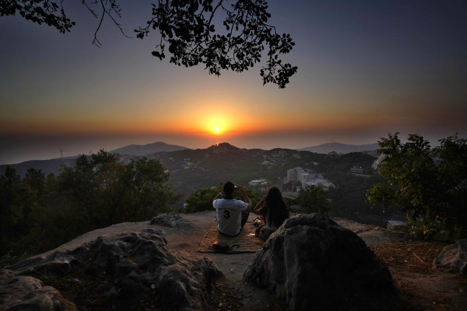 A young couple enjoy the sunset during a hike trip in Chahtoul village, in the Keserwan district, Mount Lebanon Governorate of Lebanon, Sunday, June 27, 2021. With their dollars trapped in the bank, a lack of functioning credit cards and travel restrictions imposed because of the pandemic, many Lebanese who traditionally vacationed over the summer at regional hotspots are also now turning toward domestic tourism. (AP Photo/Hassan Ammar)