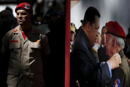 A soldier stands next to a portrait of Venezuela's late President Hugo Chavez at the Plaza Bolivar near the building housing the National Assembly in Caracas, January 7, 2016. REUTERS/Marco Bello