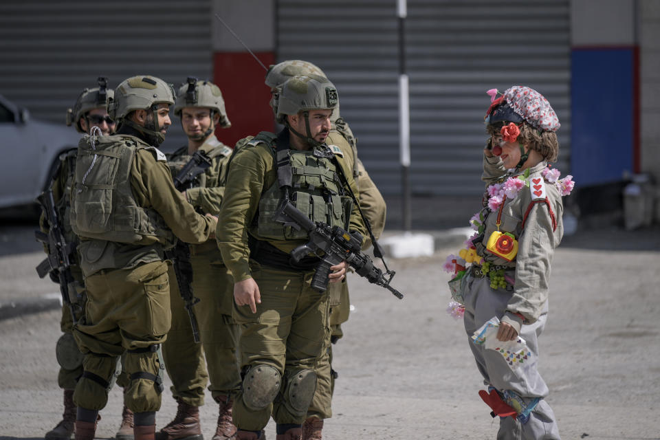 An Israeli activist dressed as a clown salutes to a group of Israeli soldiers during a solidarity rally by Israeli left-wing activists in the West Bank town of Hawara which was set ablaze by radical Jewish settlers earlier this week, Friday, March 3, 2023. On Monday scores of Israeli settlers have gone on a violent rampage in the northern West Bank town of Hawara, setting cars and homes on fire after two settlers were killed by a Palestinian gunman. (AP Photo/Majdi Mohammed)