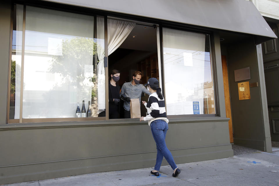 In this Thursday, June 18, 2020, photo, lead sommelier Rachel Coe, left, and service manager Antoine Mueller wear face masks as they assist a customer at the Atelier Crenn restaurant window during the coronavirus outbreak in San Francisco. Some of the world's best restaurants have had to make a quick pivot to weather the coronavirus. (AP Photo/Jeff Chiu)