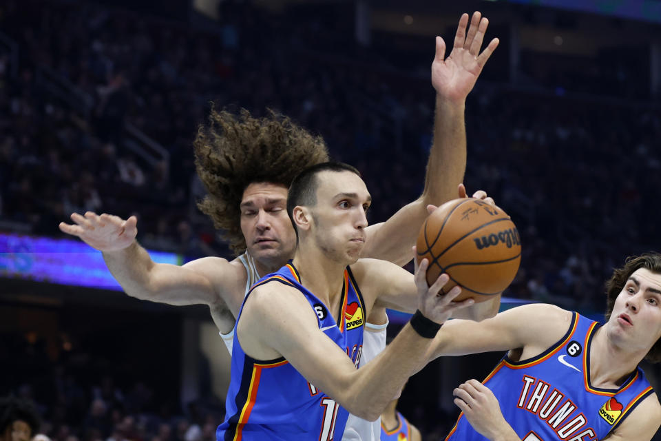 Oklahoma City Thunder forward Aleksej Pokusevski (17) grabs a rebound against Cleveland Cavaliers center Robin Lopez, left, during the first half of an NBA basketball game, Saturday, Dec. 10, 2022, in Cleveland. (AP Photo/Ron Schwane)