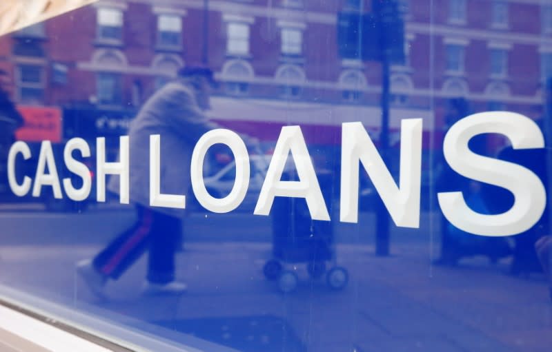FILE PHOTO: A pedestrian is reflected in a sign of a payday lending shop in London