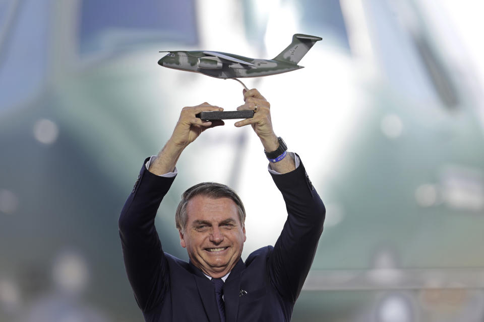 Brazil's President Jair Bolsonaro holds up a miniature of a KC-390 plane during the Brazilian Air Force delivery ceremony of the first military aircraft KC-390, at the air base in Anapolis, Brazil, Wednesday, Sept. 4, 2019. The aircraft is capable of transporting and launching cargo and troops, as well as a wide range of missions: air evacuation, search and rescue, firefighting, air refueling and humanitarian aid. (AP Photo/Eraldo Peres)