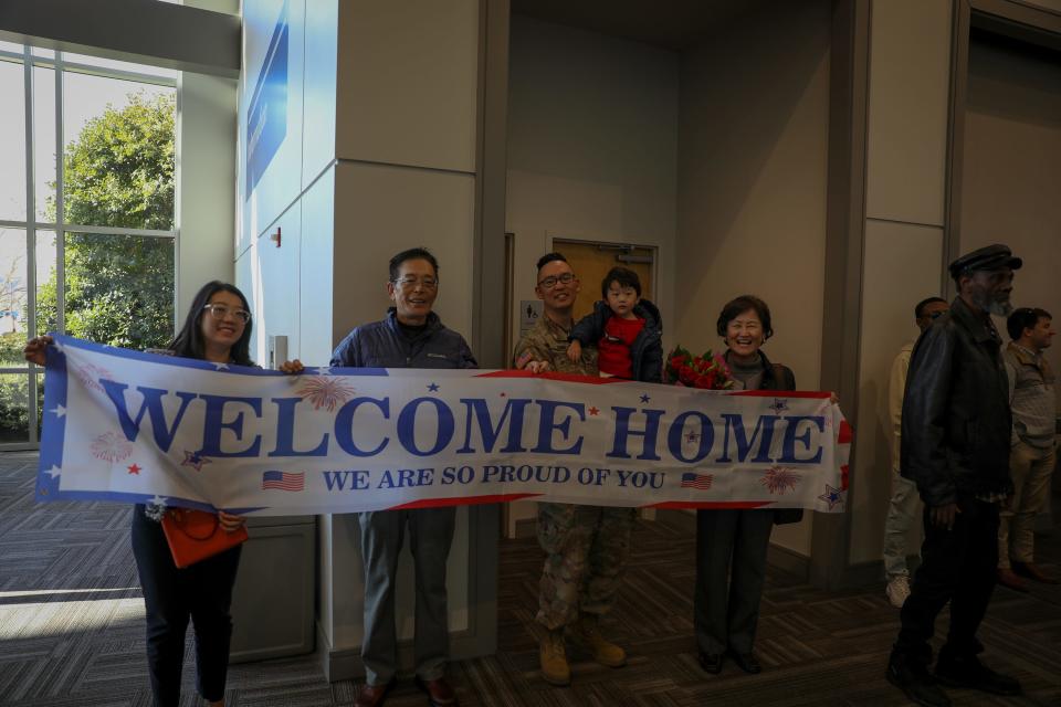 Alabama Army National Guard Captain Boem Jung stands behind a ‘welcome home’ banner with his family in Birmingham, Ala., January 14, 2023. Jung has just returned from a deployment with the 135th Expeditionary Sustainment Command in Kuwait.