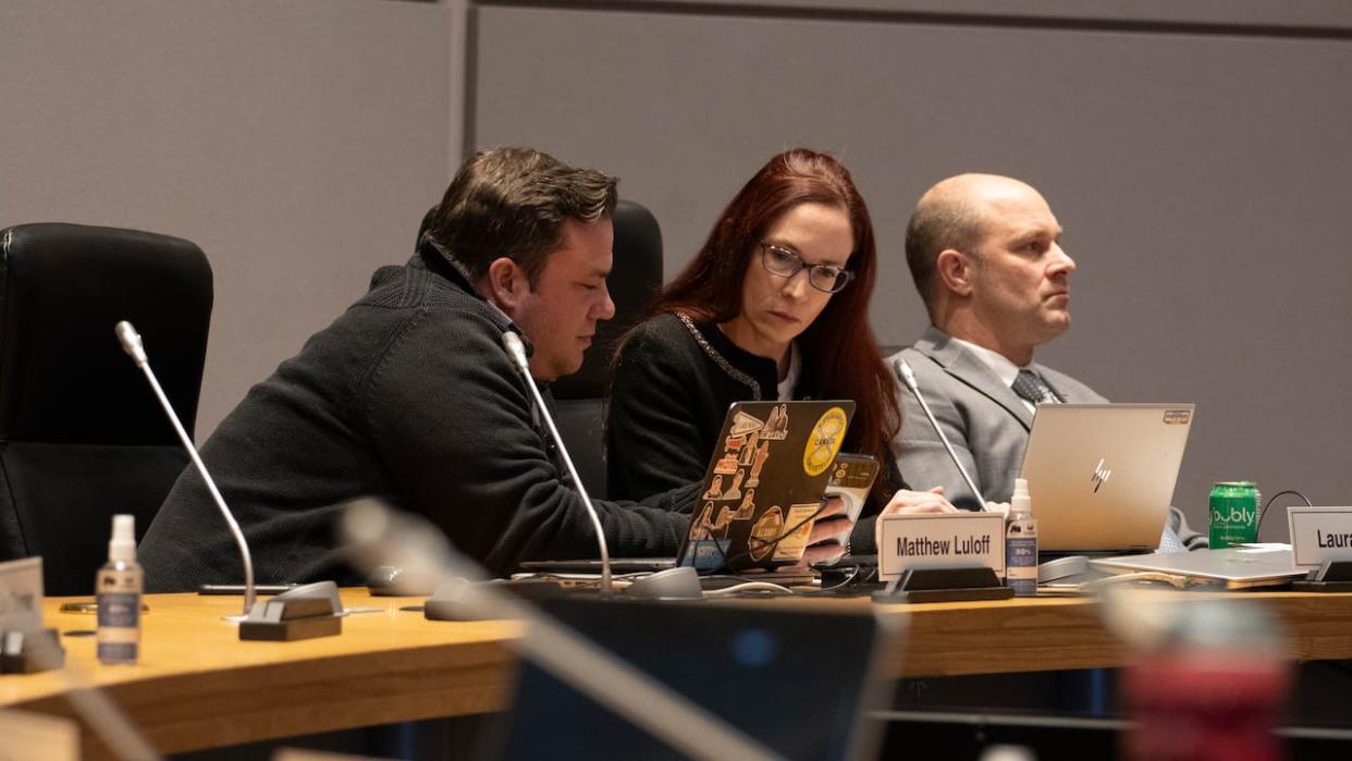 Orléans East-Cumberland Coun. Matt Luloff, left shows Orléans West-Innes Coun. Laura Dudas something on his phone, while Barrhaven West Coun. David Hill looks on at a meeting last week. Dudas and Hill want to know more about how the Groupe Katasa donation was negotiated.  (Jean Delisle/CBC - image credit)