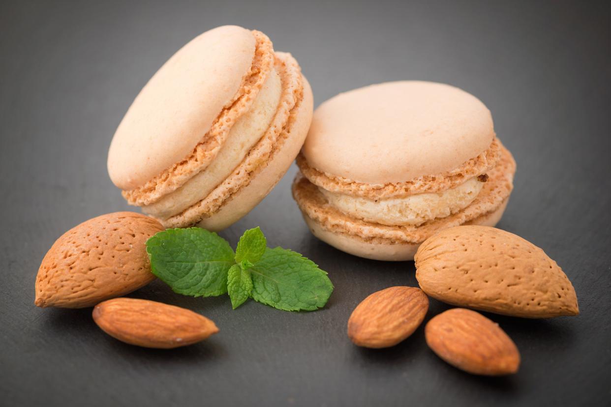 Two almond macaroons with almonds on a gradient dark grey background