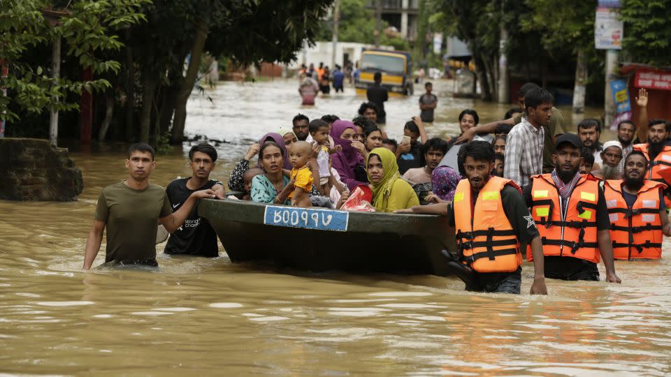 Rescuers in orange life vests escort stranded people to higher ground in Bangladesh. - CNN/Salman Saeed