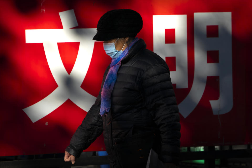 A woman wearing a face mask to protect against the coronavirus walks past a propaganda billboard with the characters for "culture" in Beijing, Friday, Nov. 20, 2020. (AP Photo/Mark Schiefelbein)