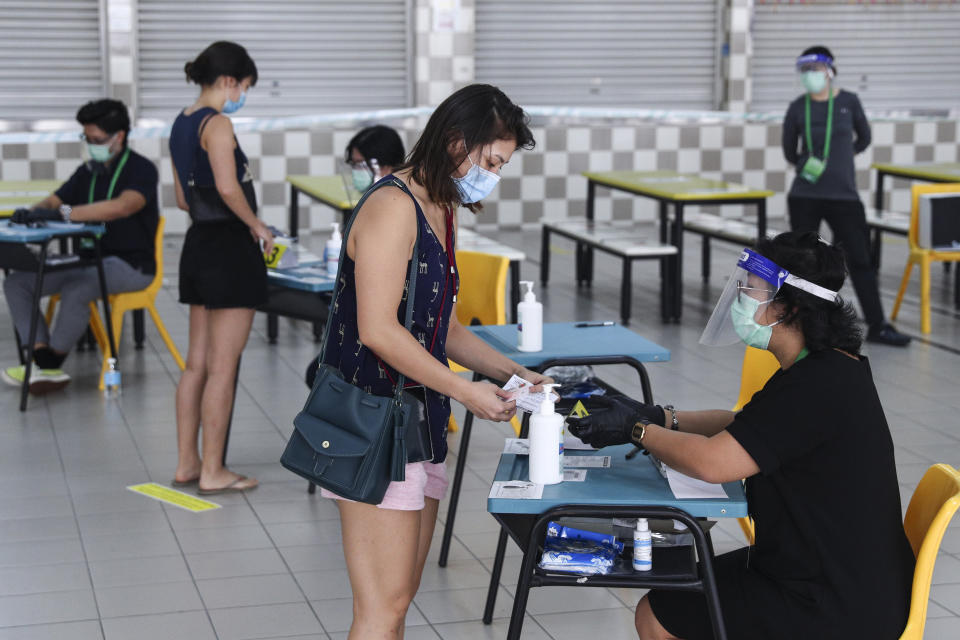 Voters, wearing face masks, verify their identities with polling officers at the Chung Cheng High School polling center before casting their votes in Singapore, Friday, July 10, 2020. Singaporeans began voting in a general election that is expected to return Prime Minister Lee Hsien Loong's long-governing party to power. (AP Photo)