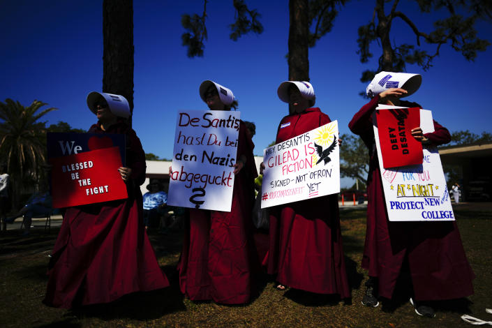 A group of parents of New College of Florida current students and one recent alum protest dressed as handmaids from Margaret Atwood's "The Handmaid's Tale," ahead of a meeting by the college's board of trustees, Tuesday, Feb. 28, 2023, in Sarasota, Fla. A sign in German addressed to Florida Governor Ron DeSantis, reads, "DeSantis, Are you copying the Nazis?" The conservative-dominated board of trustees of Florida's public honors college was meeting Tuesday to take up a measure making wholesale changes in the school's diversity, equity and inclusion programs and offices.(AP Photo/Rebecca Blackwell)