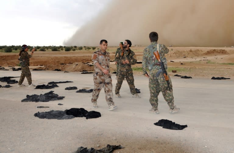 Fighters from the Syrian Democratic Forces (SDF) walk along a road dotted with black veils ditched by women after they crossed over from Islamic State group territory near Tishreen Farms, on the northern outskirts of Raqa on May 2, 2017