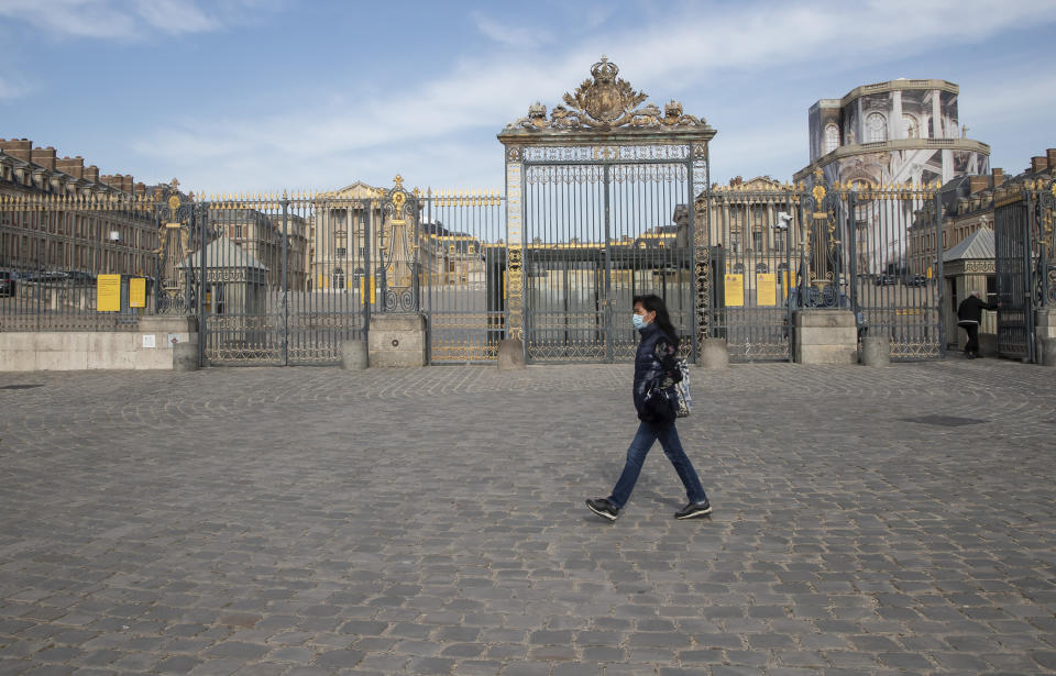 FILE - In this April 21, 2020 file photo, a woman walks past the closed Chateau de Versailles, west of Paris. Iconic sites that are among some of France's biggest tourist draws won't reopen when the country lifts most of its coronavirus restrictions next week. Neither the Louvre Museum, the Eiffel Tower nor the Versailles Palace will be reopening next week when France lifts many of its remaining coronavirus lockdown restrictions. (AP Photo/Michel Euler, File)