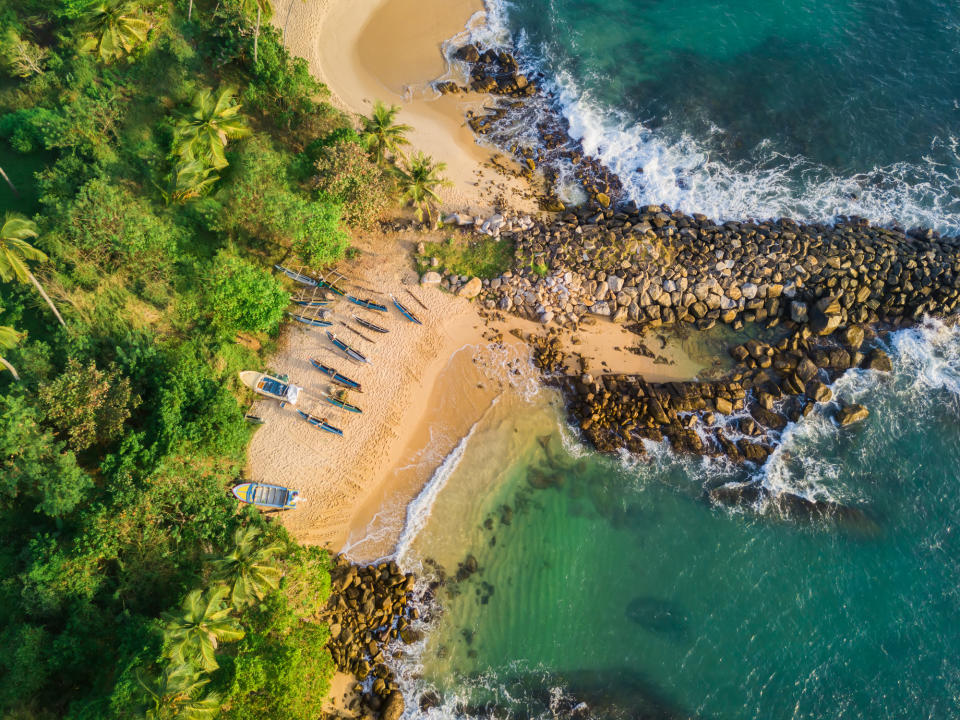 Aerial view of a beach with boats, rock barrier, and surrounding greenery