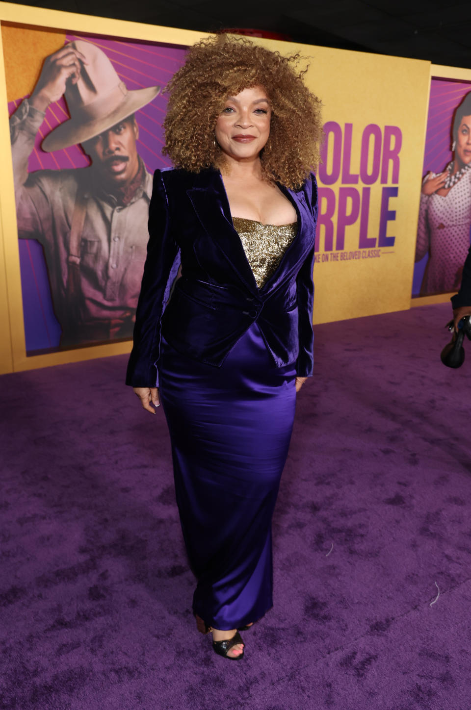 Ruth in a purple velvet suit jacket, satiny long purple gown, and sparkly gold top